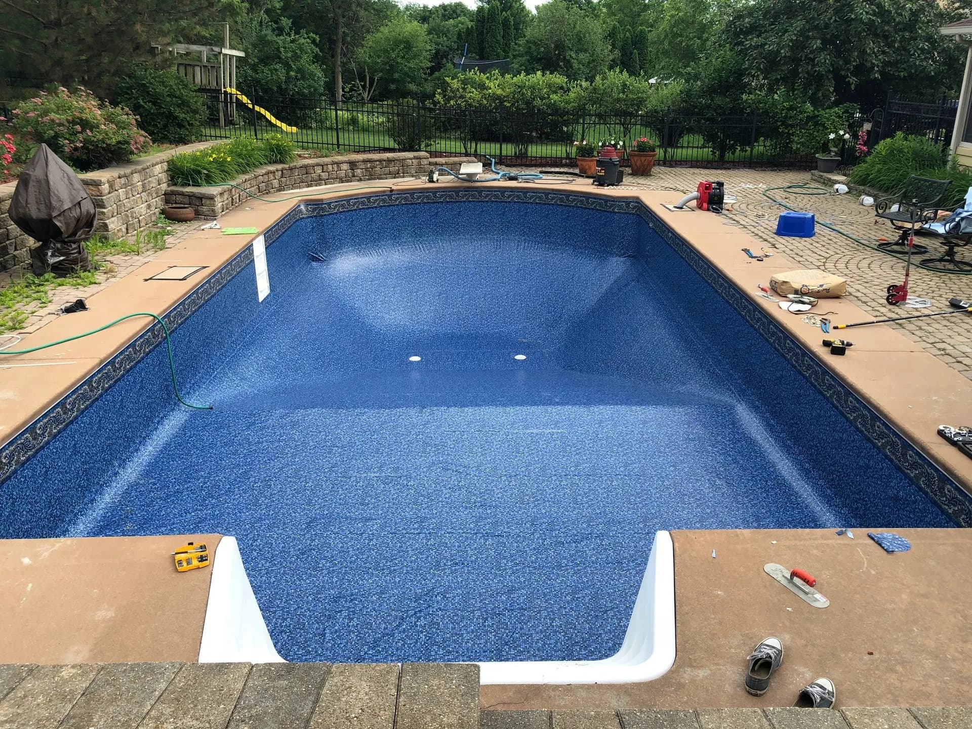 New blue vinyl pool liner set into the same pool, with the step unit fitted and materials still on the deck