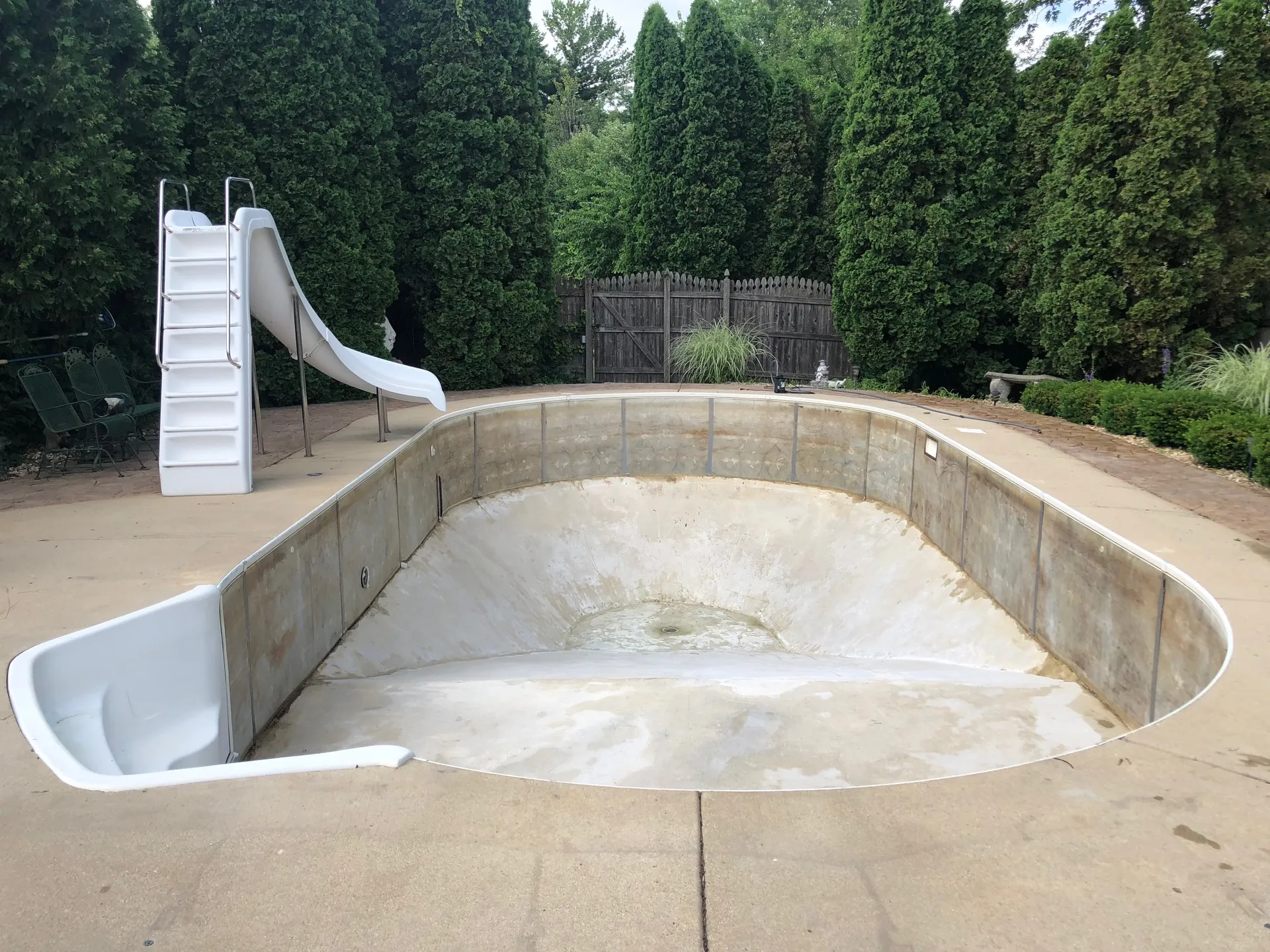 Drained inground pool with a stained concrete shell and exposed wall panels before renovation