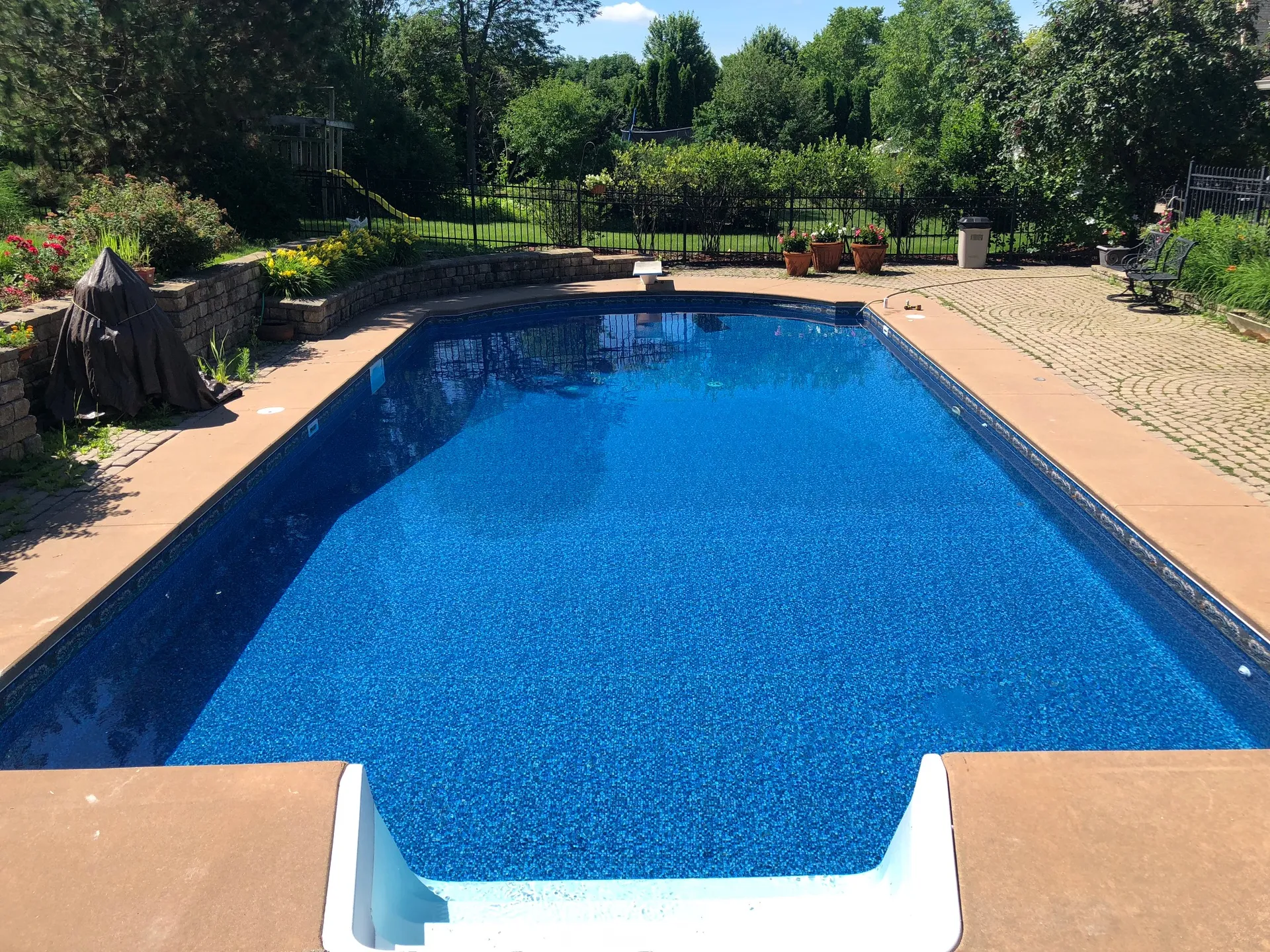Inground pool with a stone retaining wall, paver patio, and mature landscaping in the Fox Valley, Illinois